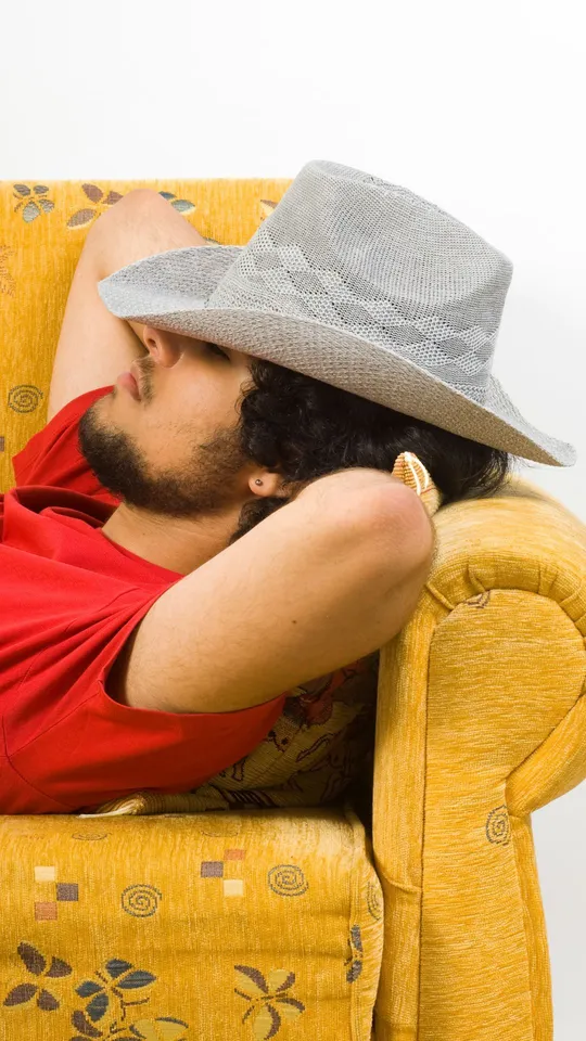 Uomo con barba e cappello che riposa su un divano giallo
